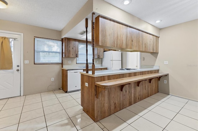 kitchen with a textured ceiling, light tile patterned flooring, a breakfast bar area, kitchen peninsula, and white appliances