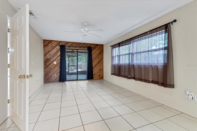 spare room featuring wood walls, ceiling fan, light tile patterned floors, and a textured ceiling