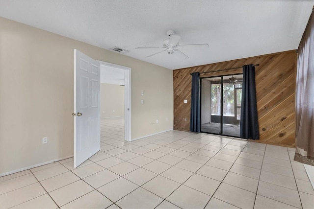 spare room featuring wooden walls, ceiling fan, and light tile patterned floors