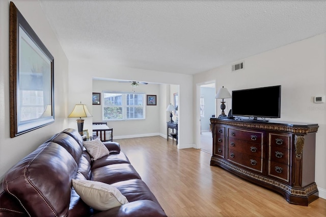 living room featuring ceiling fan, a textured ceiling, and light wood-type flooring