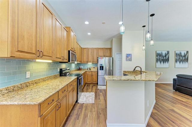 kitchen featuring light hardwood / wood-style floors, light stone counters, pendant lighting, stainless steel appliances, and a kitchen island with sink