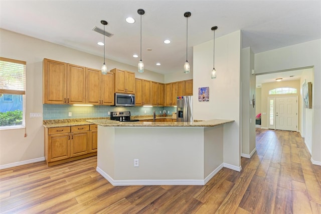 kitchen with light stone countertops, stainless steel appliances, light hardwood / wood-style floors, and pendant lighting