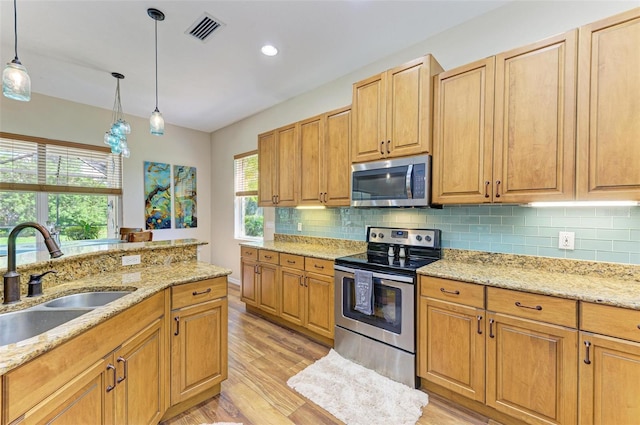 kitchen featuring sink, hanging light fixtures, light hardwood / wood-style flooring, stainless steel appliances, and light stone countertops