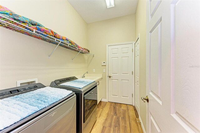 laundry area with cabinets, light wood-type flooring, washer and dryer, and sink