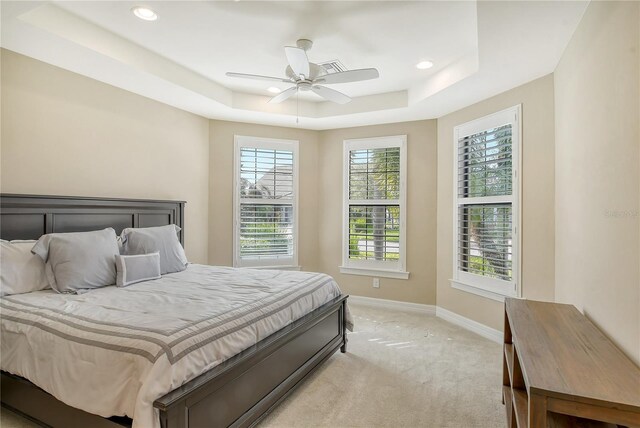 bedroom with light carpet, ceiling fan, and a raised ceiling