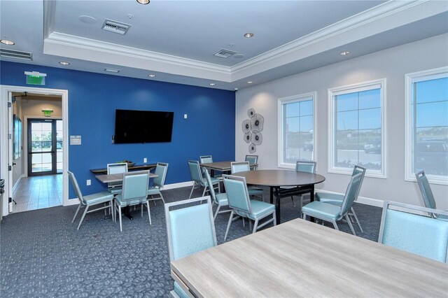 dining area featuring a tray ceiling, crown molding, dark colored carpet, and a healthy amount of sunlight