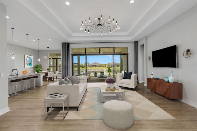 living room featuring an inviting chandelier, light wood-type flooring, and a tray ceiling