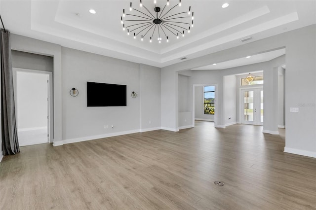 unfurnished living room with a raised ceiling, light wood-type flooring, and a chandelier