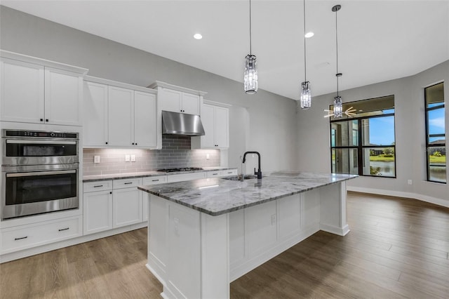 kitchen featuring a kitchen island with sink, sink, white cabinets, hanging light fixtures, and stainless steel appliances