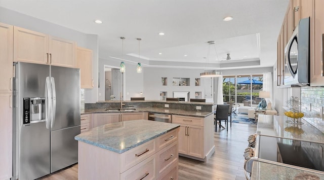 kitchen featuring a raised ceiling, kitchen peninsula, decorative light fixtures, light hardwood / wood-style flooring, and stainless steel appliances