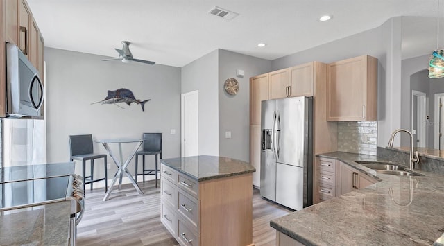 kitchen featuring appliances with stainless steel finishes, dark stone countertops, light brown cabinets, light hardwood / wood-style flooring, and sink