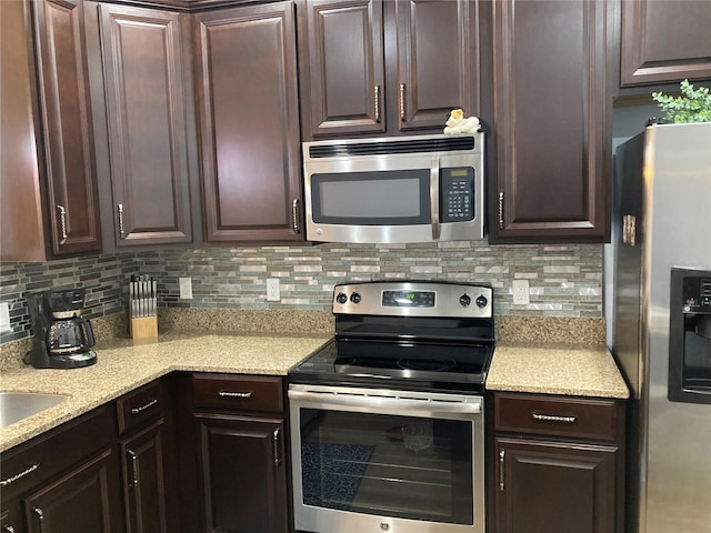 kitchen featuring appliances with stainless steel finishes, dark brown cabinets, light stone counters, and tasteful backsplash