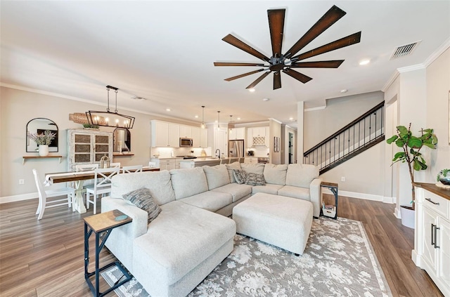 living room featuring sink, ceiling fan with notable chandelier, crown molding, and hardwood / wood-style floors