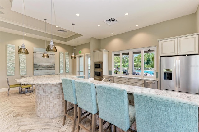 kitchen with light stone counters, hanging light fixtures, white cabinetry, stainless steel appliances, and a breakfast bar area