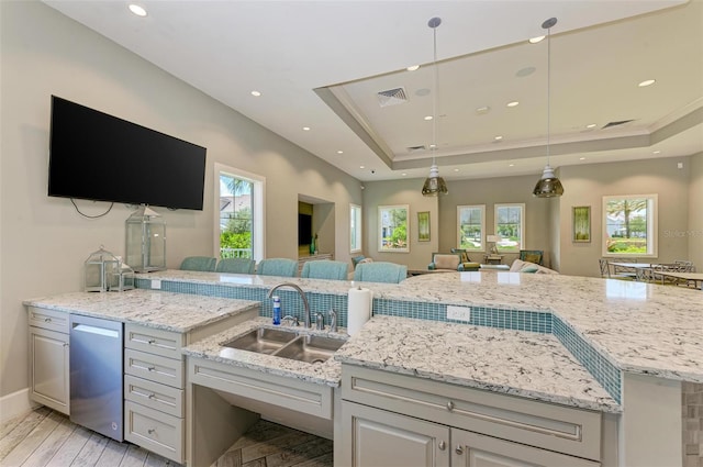 kitchen featuring light hardwood / wood-style floors, dishwasher, a tray ceiling, decorative light fixtures, and sink