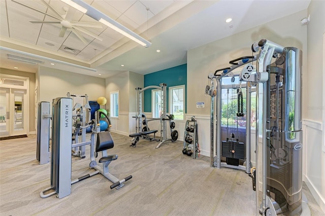 gym featuring light carpet, a tray ceiling, and ceiling fan