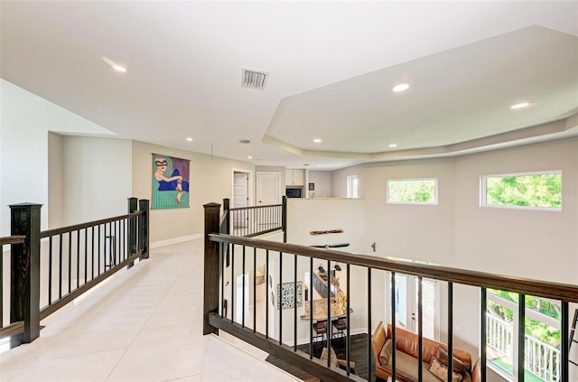 hallway featuring light tile patterned floors and a tray ceiling