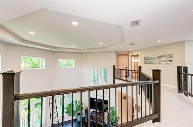 hallway with light tile patterned flooring and a raised ceiling