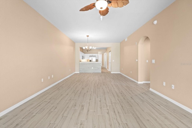 unfurnished living room with light wood-style floors, arched walkways, baseboards, and ceiling fan with notable chandelier