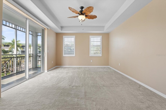 empty room with a tray ceiling, light colored carpet, ceiling fan, and baseboards