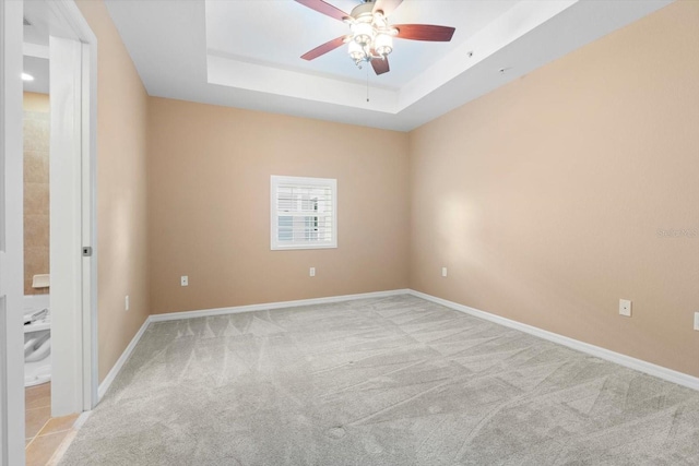 unfurnished room featuring a raised ceiling, light colored carpet, and ceiling fan