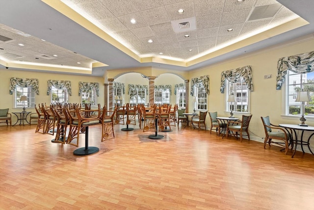 misc room with ornate columns, a raised ceiling, a paneled ceiling, and light wood-type flooring