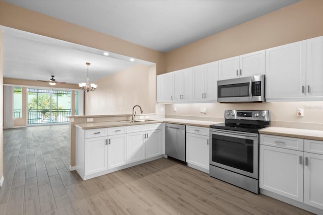 kitchen featuring stainless steel appliances, light wood-type flooring, hanging light fixtures, sink, and white cabinetry