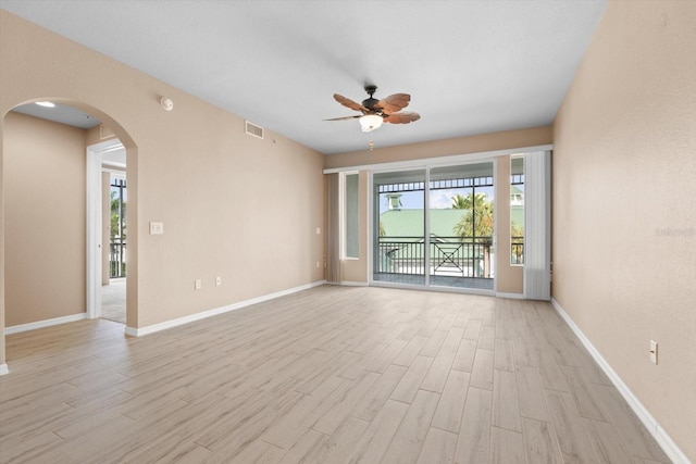 spare room featuring baseboards, visible vents, arched walkways, a ceiling fan, and light wood-style flooring