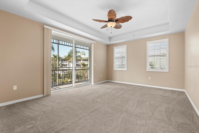 unfurnished room featuring a raised ceiling, light colored carpet, and ceiling fan