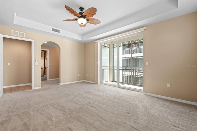 spare room featuring arched walkways, a raised ceiling, visible vents, and baseboards