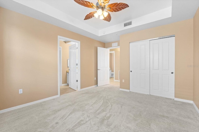 unfurnished bedroom with a closet, ceiling fan, a tray ceiling, and light colored carpet