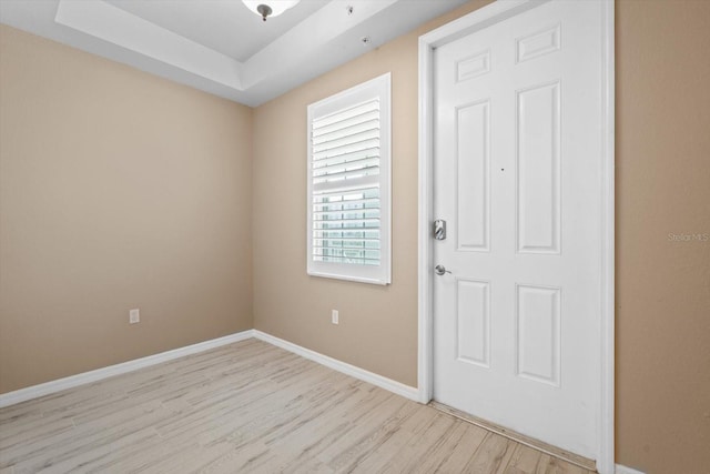 entryway with light wood-style flooring, baseboards, and a tray ceiling