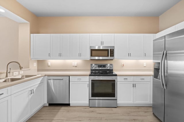 kitchen with a sink, white cabinetry, stainless steel appliances, and light countertops