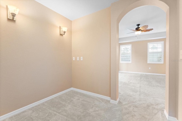 hallway featuring arched walkways, light carpet, and baseboards