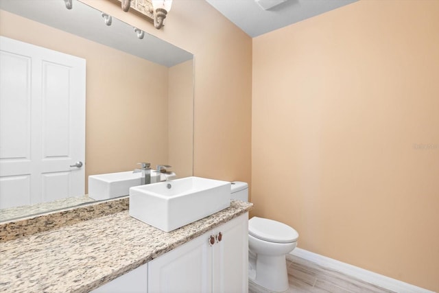 half bathroom with toilet, baseboards, wood finished floors, and vanity