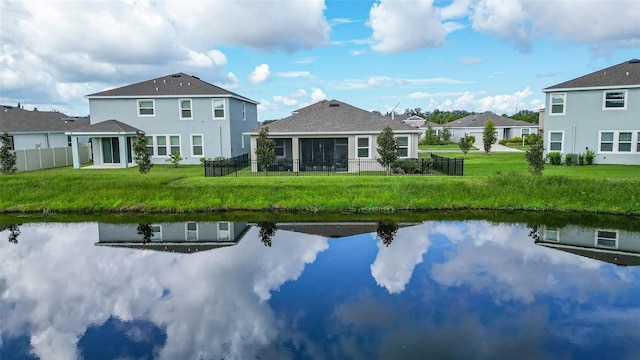 rear view of property featuring a sunroom, a water view, and a lawn