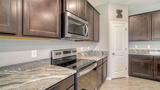 kitchen featuring dark brown cabinetry, light stone counters, light tile patterned flooring, and stainless steel appliances