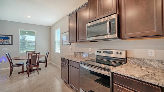 kitchen with dark brown cabinetry, light stone counters, light tile patterned flooring, and appliances with stainless steel finishes