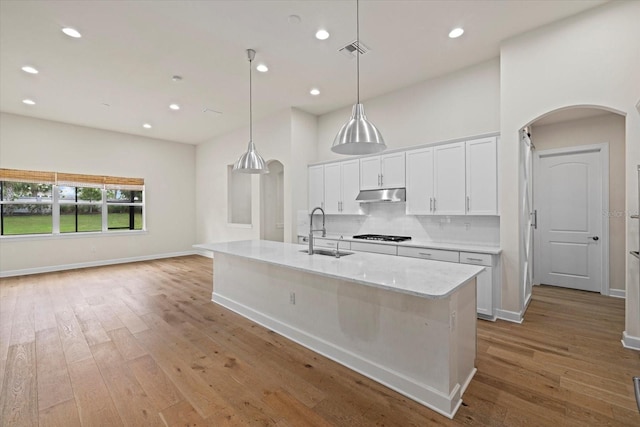 kitchen featuring pendant lighting, sink, a kitchen island with sink, white cabinetry, and light wood-type flooring