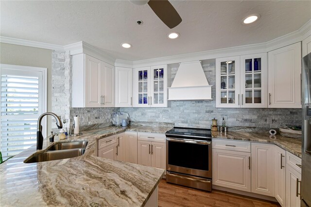 kitchen with premium range hood, white cabinetry, stainless steel range with electric cooktop, and sink