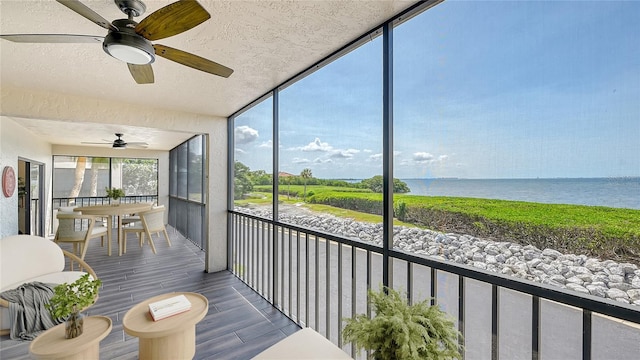 sunroom with ceiling fan and a water view