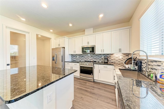 kitchen with a kitchen island, light hardwood / wood-style flooring, white cabinetry, stainless steel appliances, and dark stone countertops