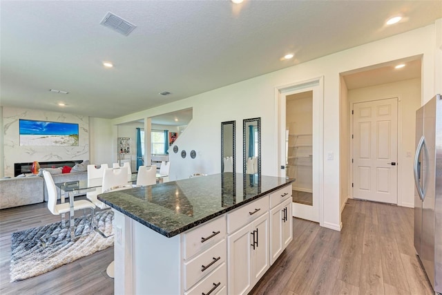 kitchen featuring white cabinets, stainless steel fridge, hardwood / wood-style flooring, dark stone countertops, and a fireplace