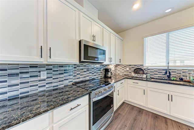 kitchen with white cabinets, sink, appliances with stainless steel finishes, dark stone countertops, and hardwood / wood-style floors