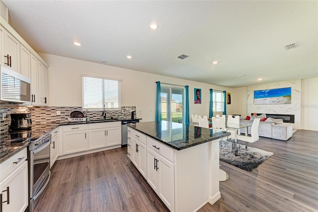 kitchen featuring appliances with stainless steel finishes, dark stone countertops, white cabinets, a fireplace, and dark hardwood / wood-style floors