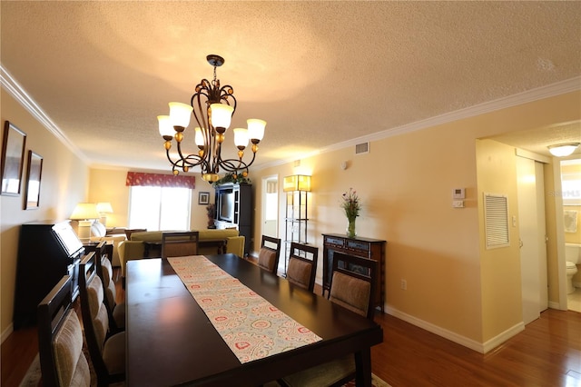 dining area with wood-type flooring, a textured ceiling, crown molding, and a notable chandelier