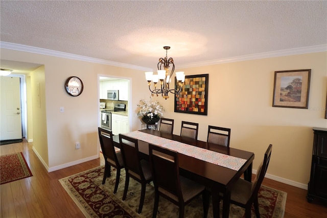 dining space with a textured ceiling, wood-type flooring, ornamental molding, and an inviting chandelier