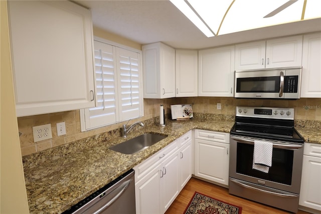 kitchen with sink, light hardwood / wood-style flooring, stone counters, white cabinetry, and appliances with stainless steel finishes