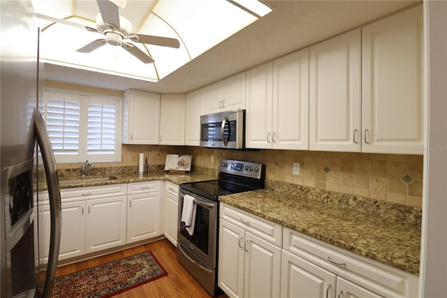 kitchen featuring wood-type flooring, white cabinets, appliances with stainless steel finishes, light stone countertops, and ceiling fan