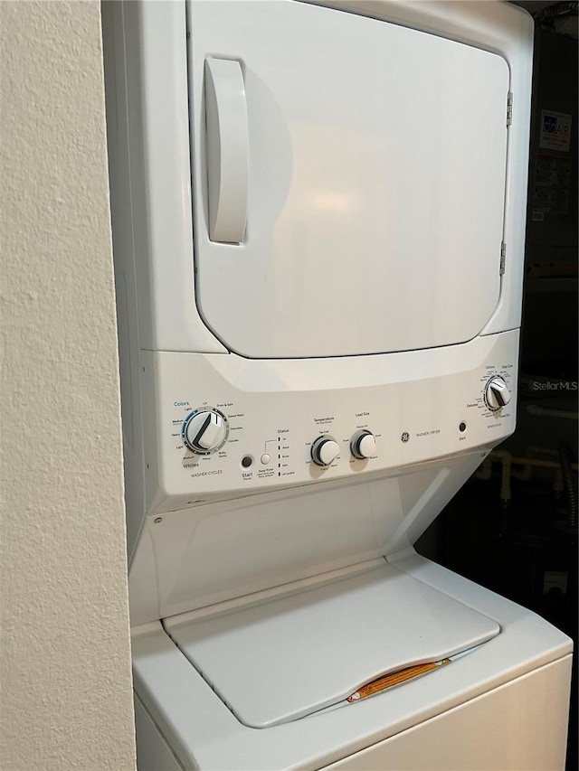laundry area with a textured wall, stacked washing maching and dryer, and laundry area
